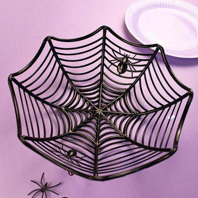 A black cobweb-patterned plastic bucket with orange accents, designed for Halloween decoration, displayed on a purple background with a white plate and spider figurines around it.
